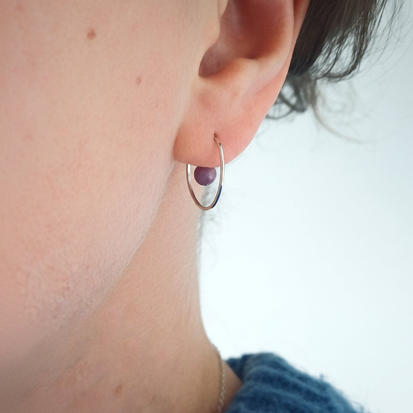 op de afbeelding die je het oor van een vrouw. ze draagt een fijne zilveren oorring met een lavendel kleurig steentje dat lijkt te zweven in het midden van de oorring. 